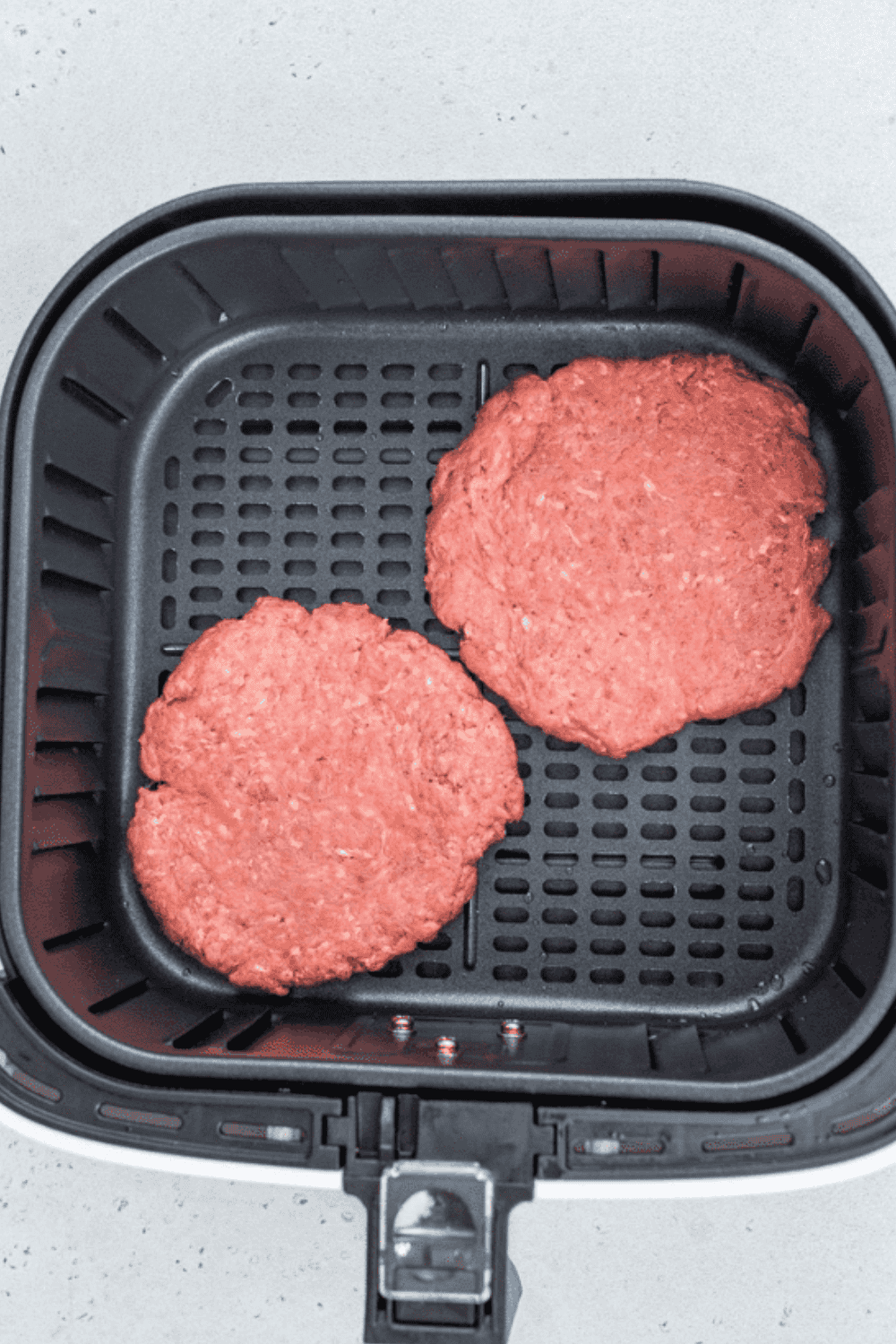 Hamburger patties cooking in an air fryer, flipped halfway for even browning.