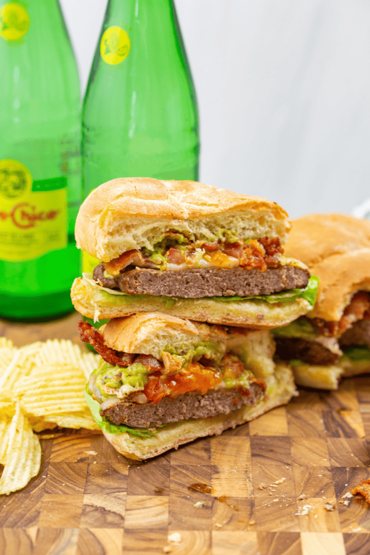 Air fryer-toasted burger buns with assembled burger including lettuce, patty, tomato, guacamole, and bacon.