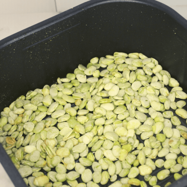 Frozen lima beans cooking in the air fryer basket with a golden crispy exterior forming during air frying