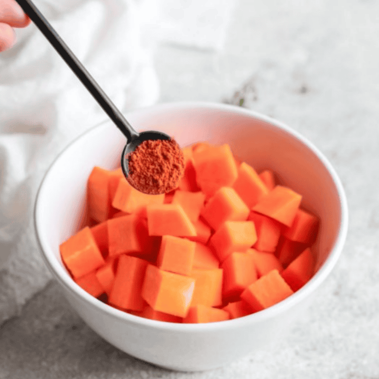 Diced pumpkin in a bowl tossed with olive oil, smoked paprika, cinnamon, salt, and pepper for air fryer roasted pumpkin