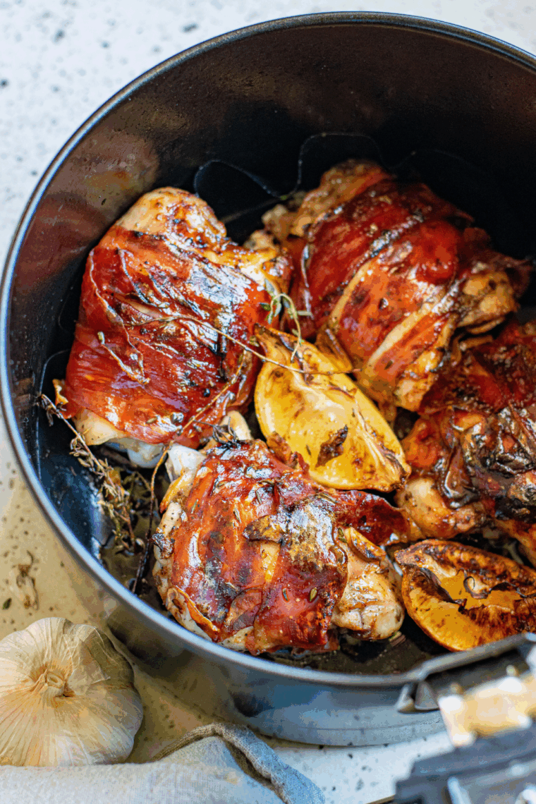 Bacon wrapped chicken thighs cooking in air fryer basket
