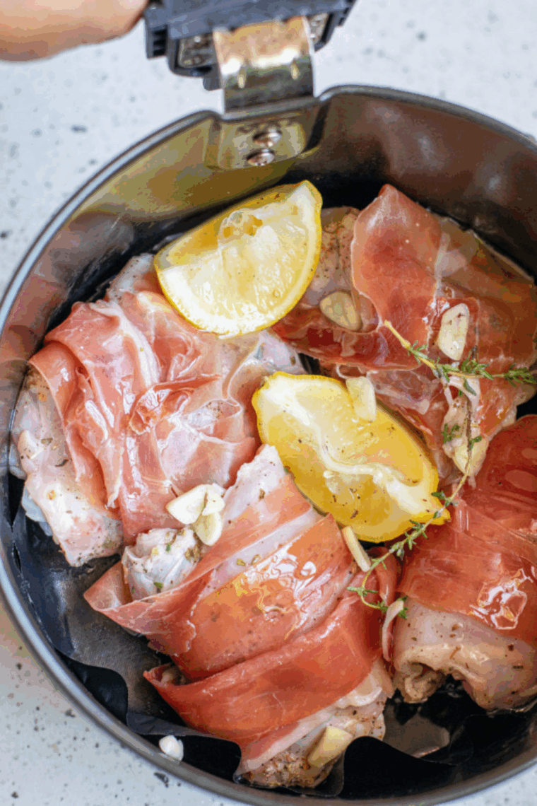 Bacon wrapped chicken thighs arranged in a single layer in air fryer basket