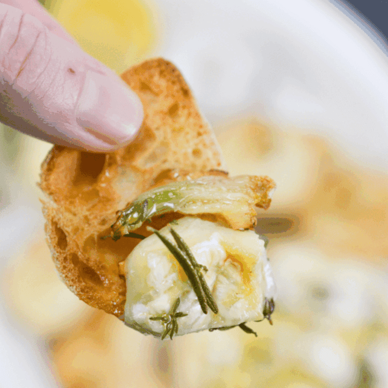 Air fryer baked Camembert topped with herbs, garlic, and honey, served warm and gooey with sliced baguette.
