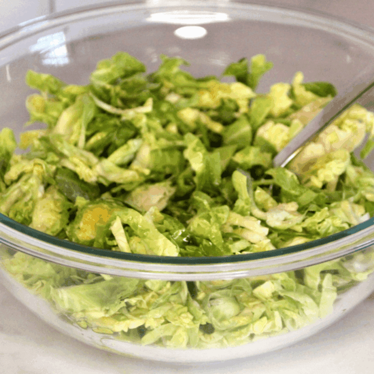 Shredded Brussels sprouts tossed with oil and seasonings in a large mixing bowl