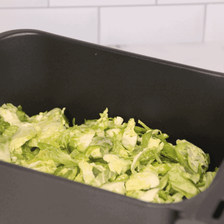 Shaved Brussels sprouts spread in a single layer in air fryer basket ready to cook at 350°F
