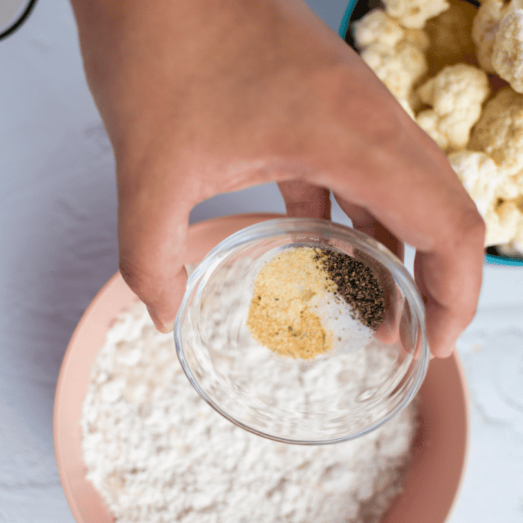 Cauliflower florets being coated in a seasoned flour and milk mixture in a large bowl.