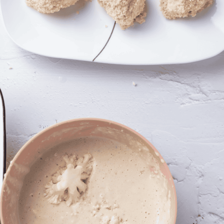 Battered cauliflower florets arranged in a single layer in the air fryer basket, lightly sprayed with cooking oil.