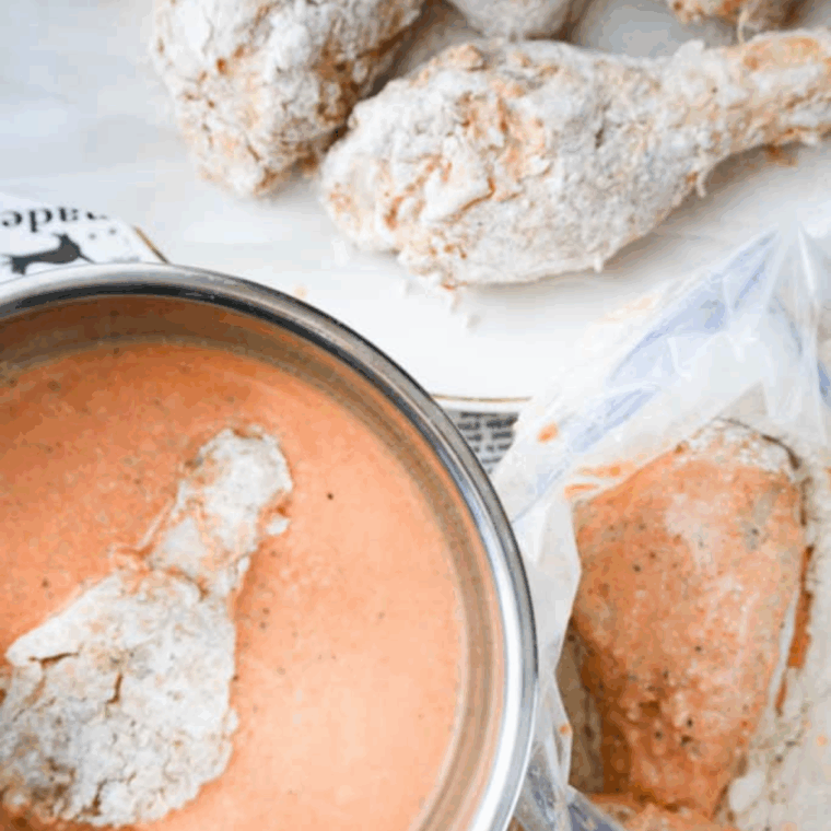 Chicken being coated in seasoned flour mixture after marinating in buttermilk