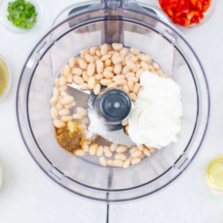 White beans, sour cream, garlic, lime juice, and cumin blended smooth in a food processor bowl"