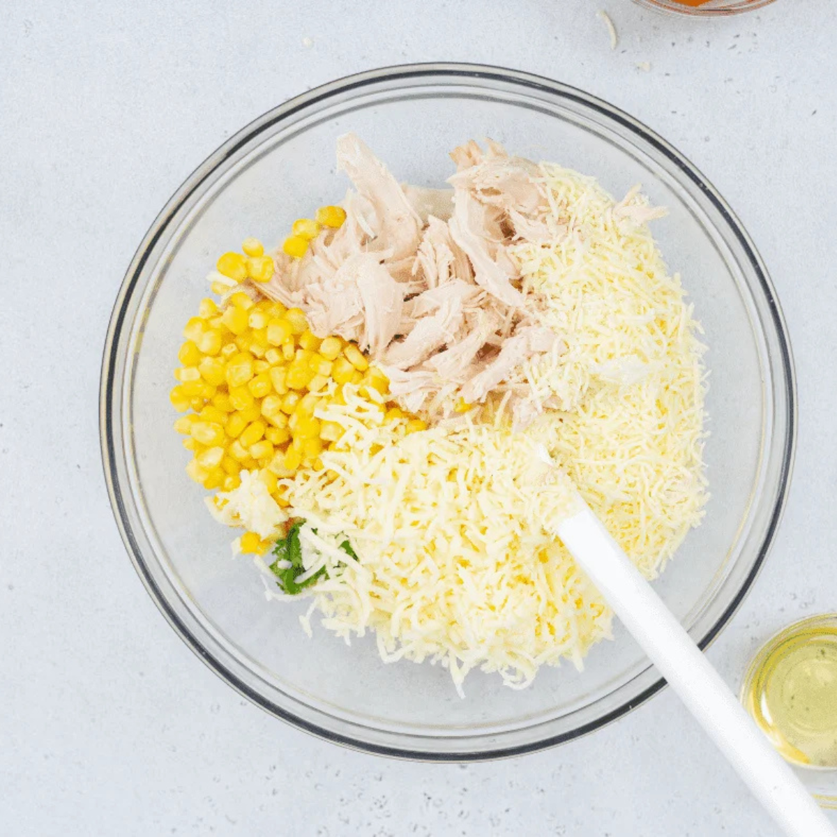 Shredded rotisserie chicken, corn, cilantro, and shredded cheese being stirred into the blended white bean base