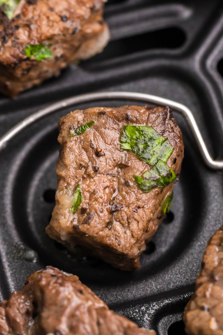 Perfectly seared steak bites coated in garlic butter sauce inside an air fryer basket, golden brown with a juicy center.