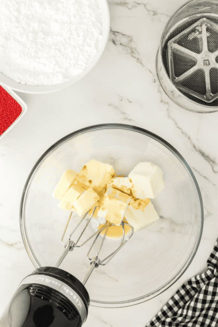 Cream cheese, butter, and powdered sugar being mixed into smooth frosting in a bowl.