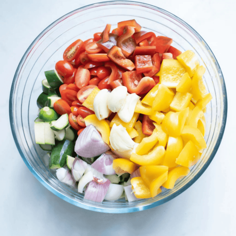 Cherry tomatoes, zucchini, red onion, garlic and bell peppers tossed with olive oil and Italian seasoning in a large mixing bowl