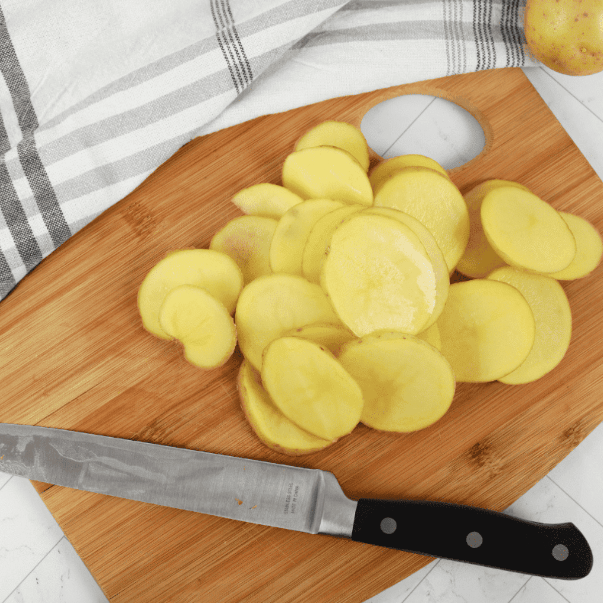 Slicing potatoes with a mandoline and sharp knife on cutting board.