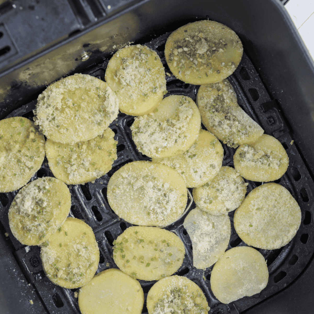 Seasoned potato slices arranged in a greased air fryer basket, cooking to crispy golden brown.