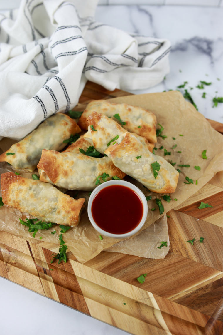 Golden chicken cilantro egg rolls on a platter beside a small dish of sweet and sour sauce