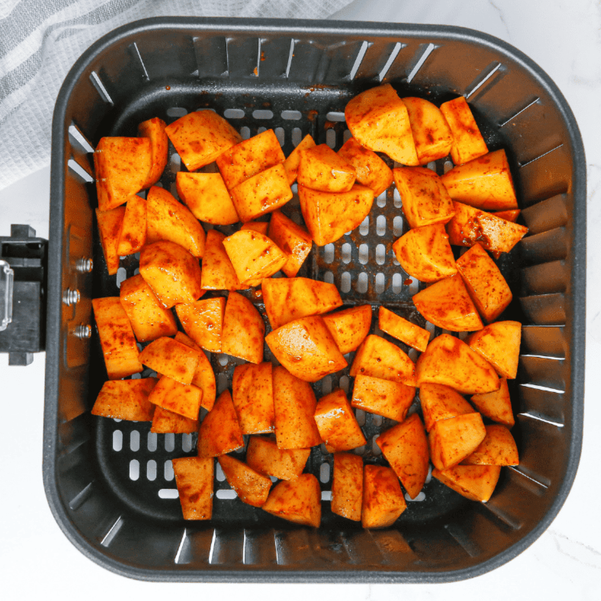 Air fryer set to 390°F with seasoned potato cubes cooking, shaken halfway for even crisping.