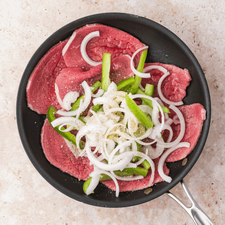 Cook the Steak and Veggies: Skillet with thinly sliced beef, green bell peppers, and onions cooking in olive oil.