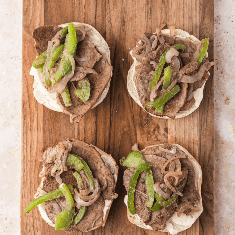 Bagel halves spread with mayonnaise, topped with cooked steak, veggies, and a slice of provolone cheese.