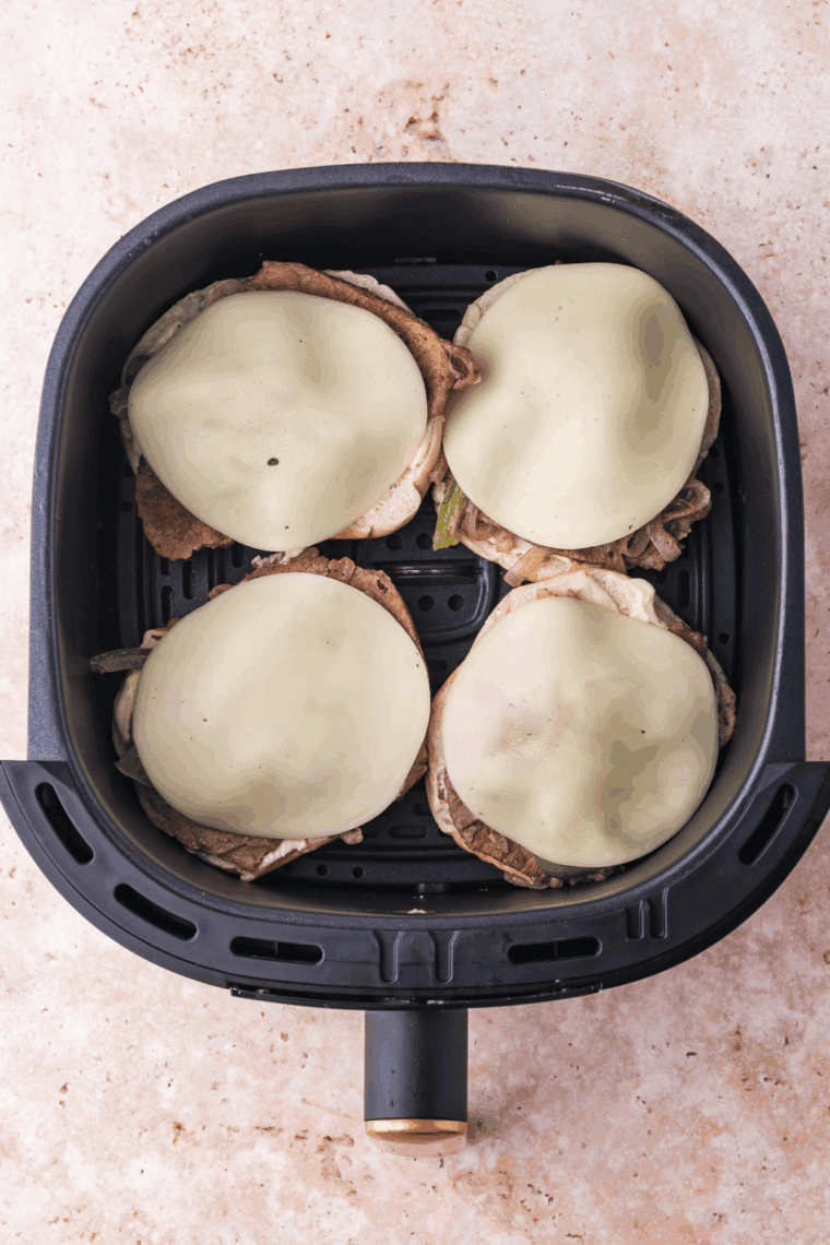Bagel halves in an air fryer basket, cheese melting and bagels toasting.