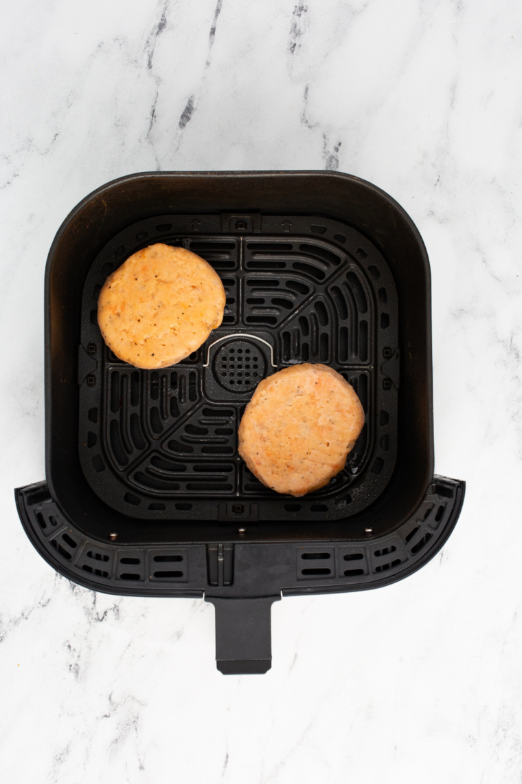 Frozen salmon patties placed in a single layer in preheated air fryer basket with cooking spray ensuring space between each patty for even crisping and proper air circulation instead of steaming