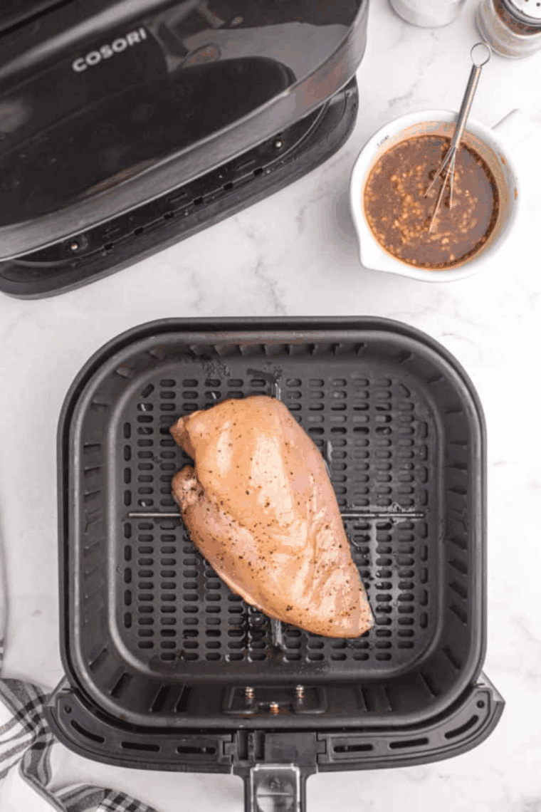 Seasoned chicken in the air fryer basket.