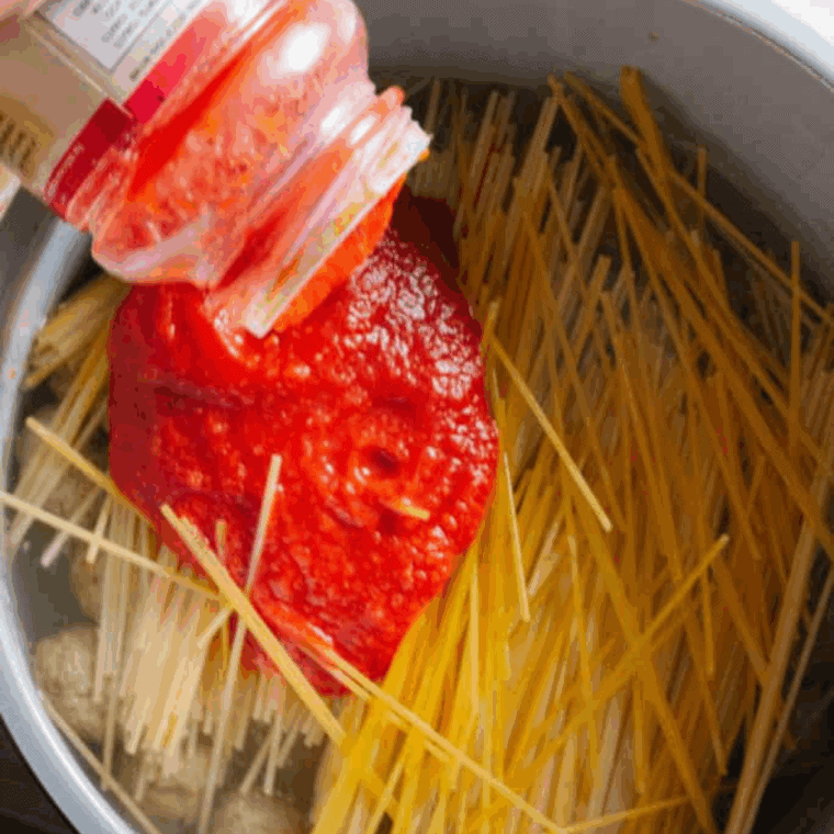 Beef broth and pasta sauce poured over broken spaghetti noodles in the Ninja Foodi, noodles arranged and submerged in the liquid.