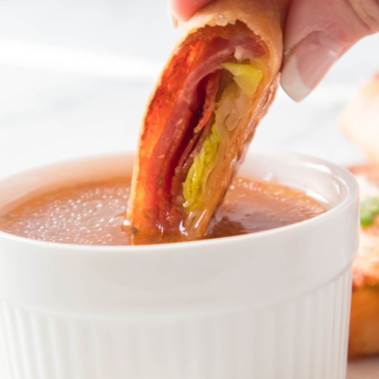 Air fryer antipasto egg roll being dipped into a bowl of Italian dressing