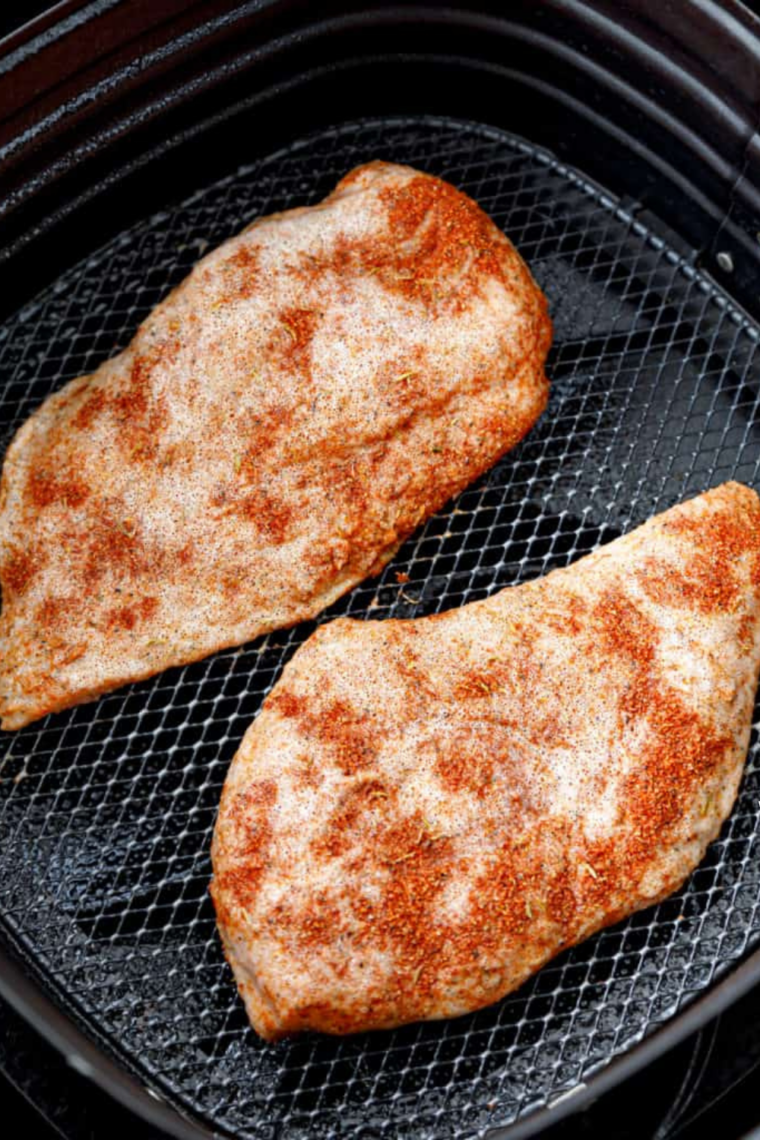 Two chicken breasts coated in blackening seasoning arranged in a single layer in an air fryer basket