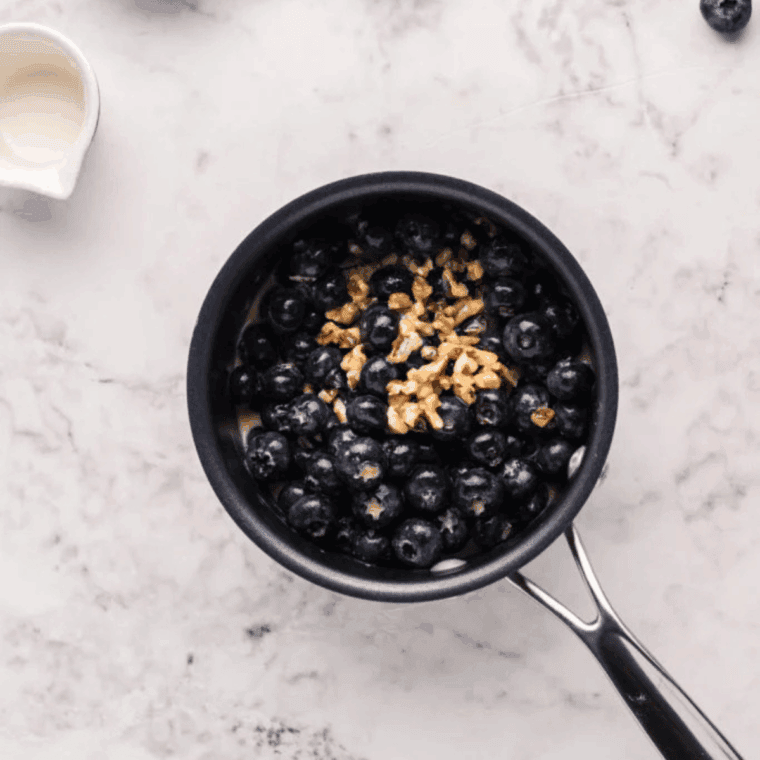 Simmering drained blueberries and walnuts with maple, cream, butter, and brown sugar in a saucepan