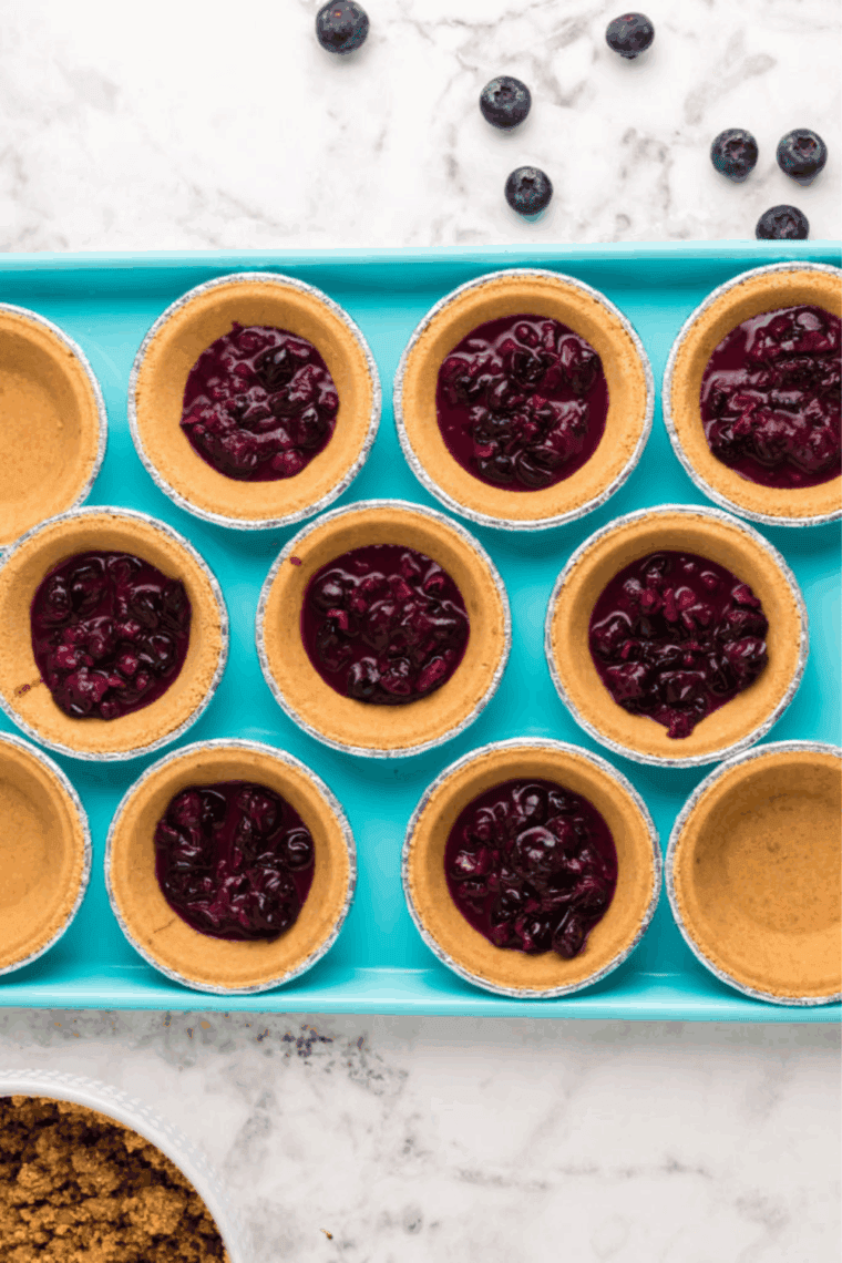Adding a scoop of blueberry mixture into each mini pie crust