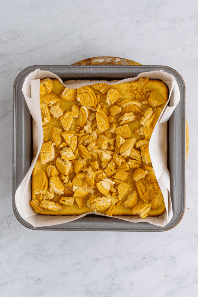Chopped golden Oreos pressed into the top of finished cheesecake bars.