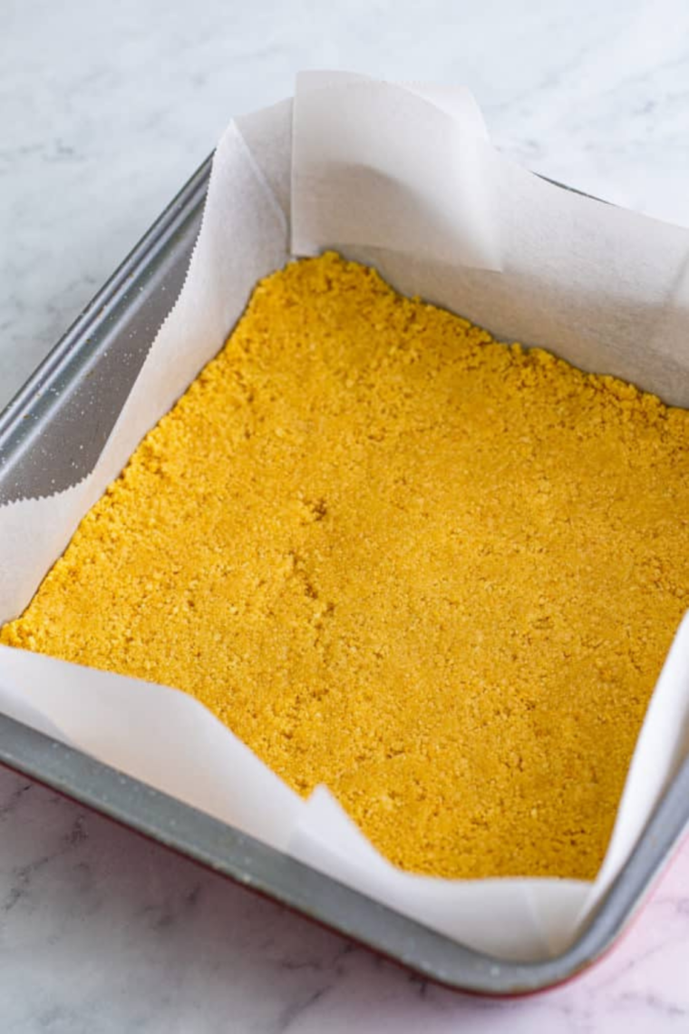  8x8 baking pan lined with parchment paper ready for cheesecake bars