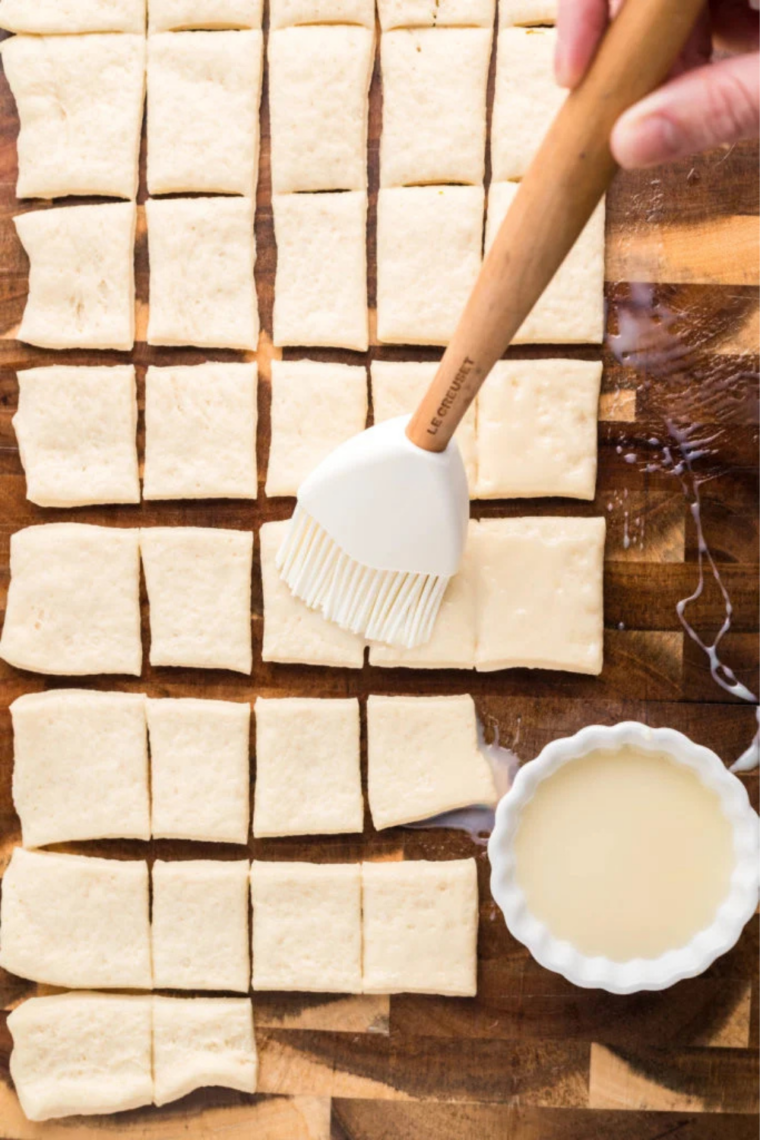 Pizza dough cut into small squares on a floured wooden cutting board