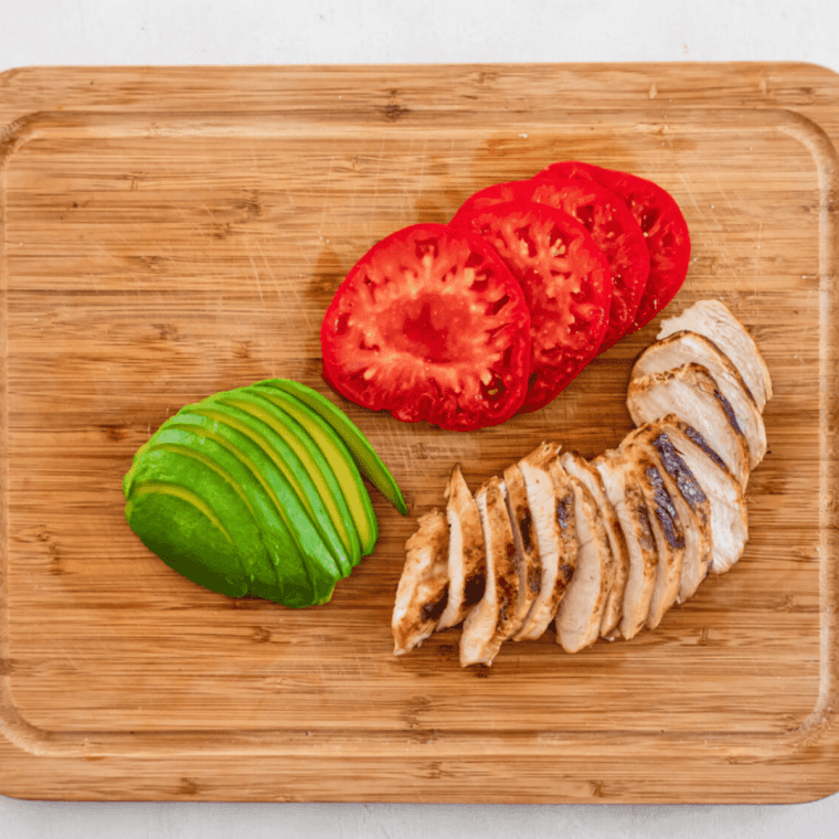 Assembling the chicken sandwich, cutting the vegetables on a cutting board.