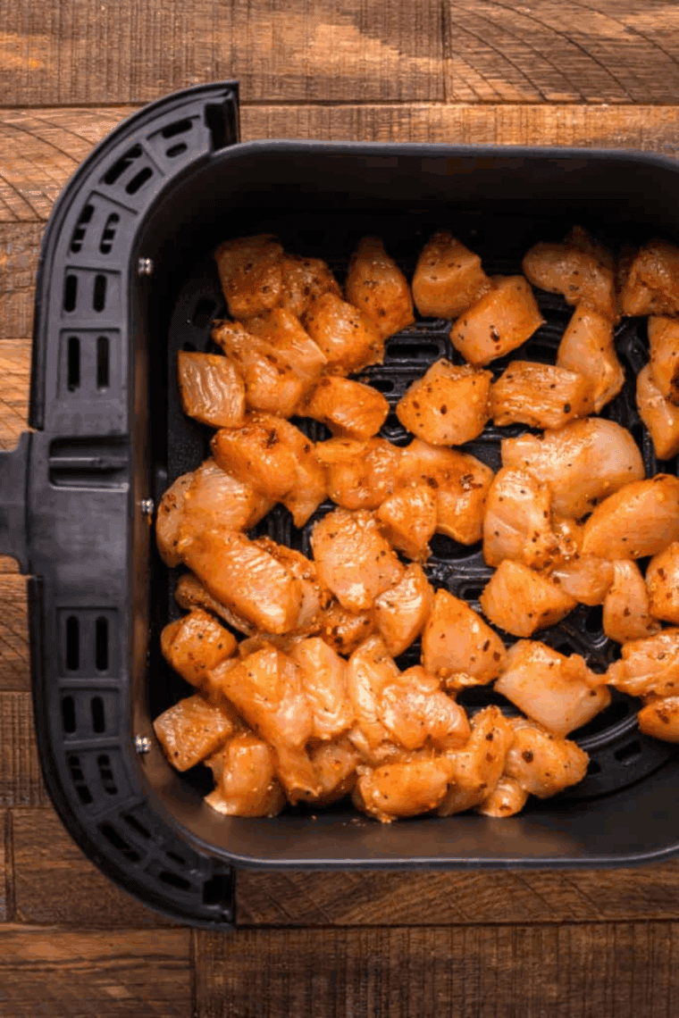 Chicken chunks in air fryer basket being coated with guava sauce before finishing cooking.