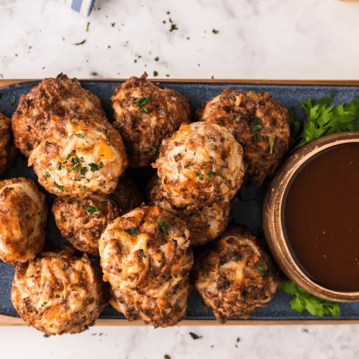 Air Fryer Sausage Balls stacked on a white plate beside a small bowl of spicy maple dipping sauce