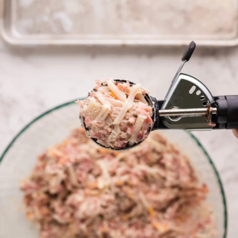 Air Fryer Sausage Balls being portioned with a cookie scoop into uniform balls on a baking sheet