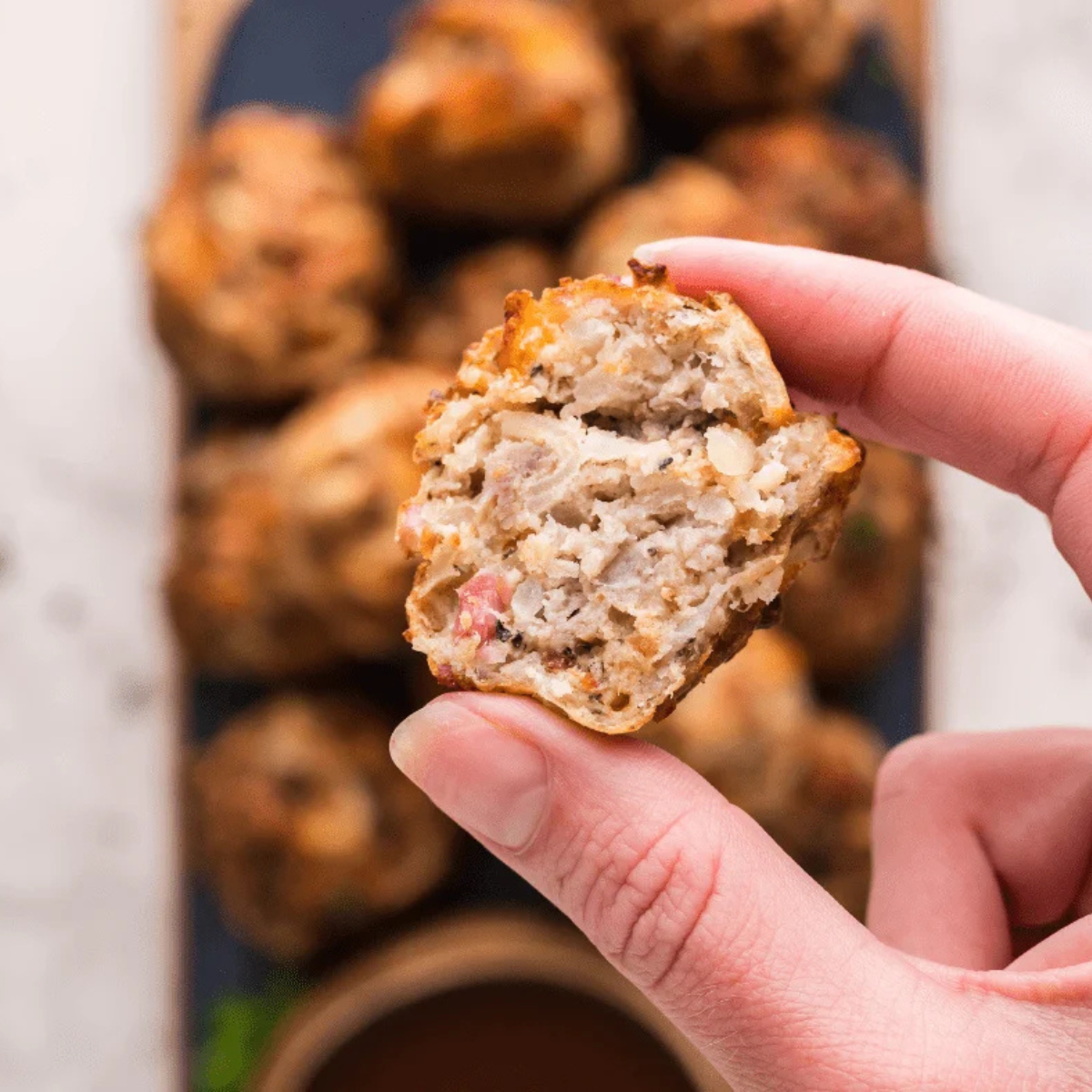 A hand holding a golden Air Fryer Sausage Ball above the platter