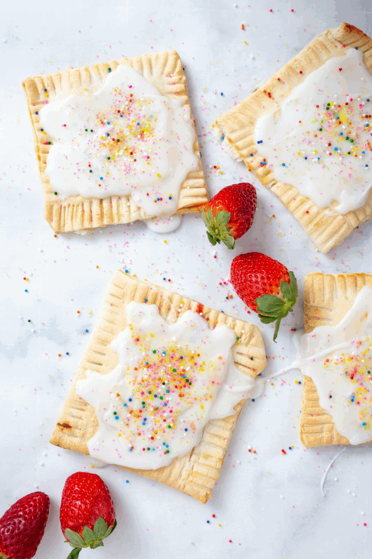 Golden, flaky air fryer strawberry pop-tarts with white icing and colorful sprinkles on a plate.
