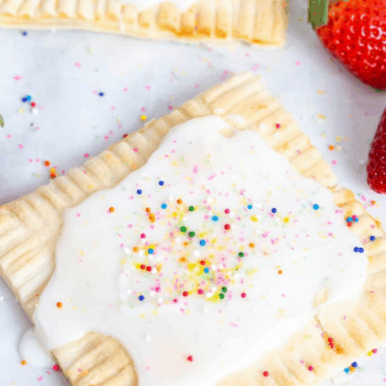 Flaky golden air fryer strawberry pop-tarts with white icing and colorful sprinkles on a white plate.