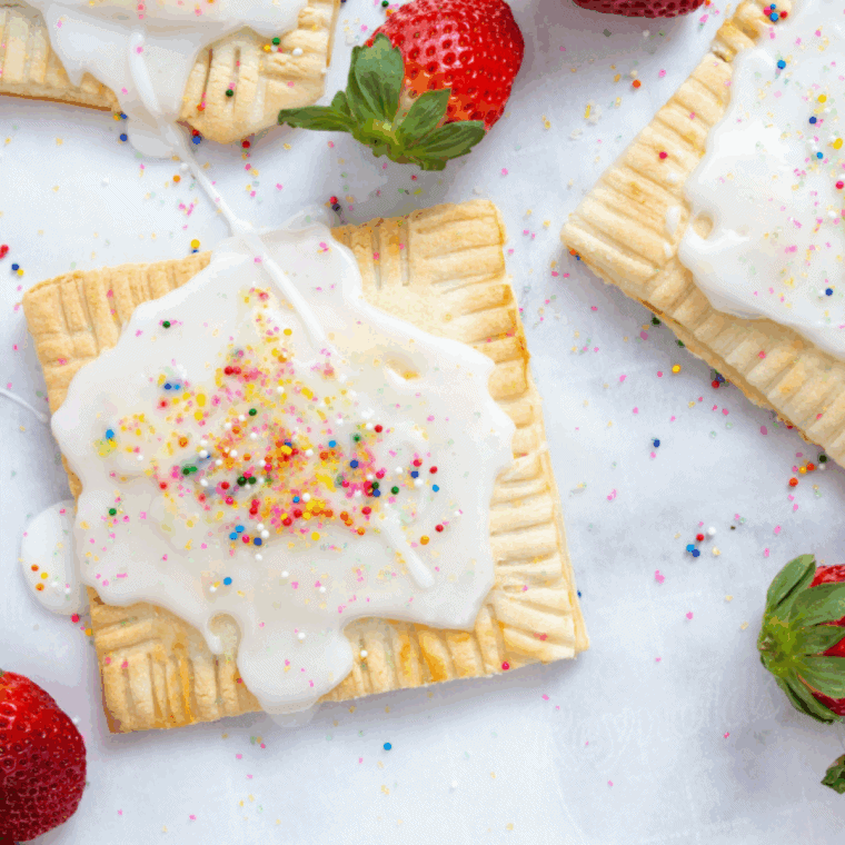 Golden air fryer strawberry pop-tarts topped with pink glaze and colorful sprinkles on a white plate.