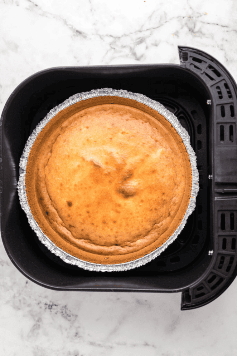 Cheesecake mixture poured into pie crust, cooking in air fryer basket at 300°F.