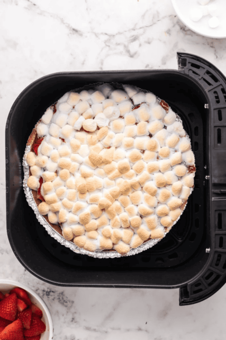 Mini marshmallows melting on top of cheesecake with strawberries in air fryer.
