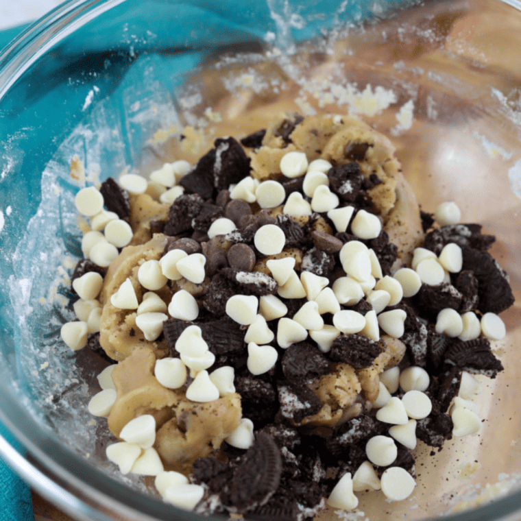 Cookie dough being mixed with milk chocolate chips, white chocolate chips, and crushed Oreos.