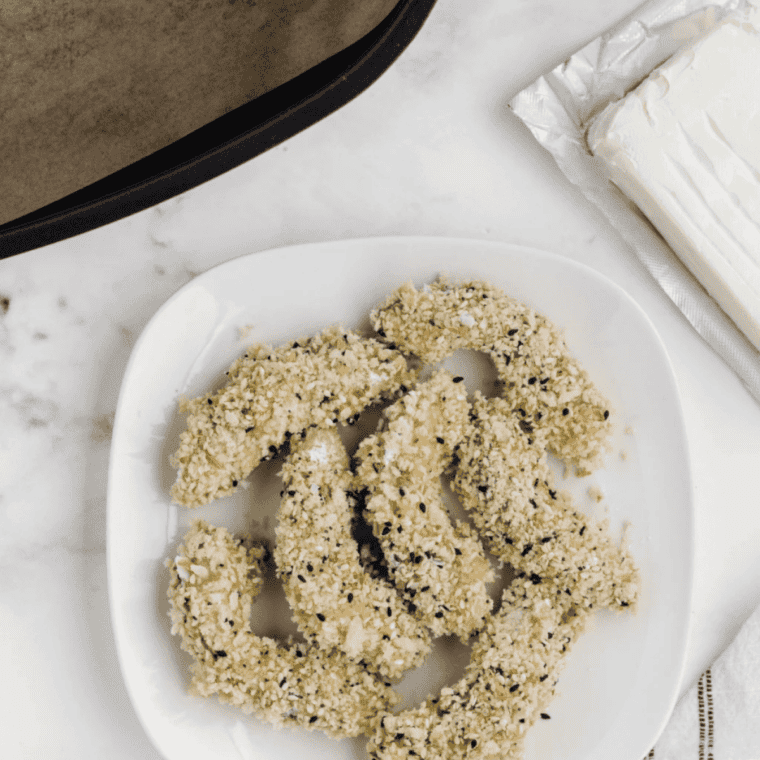 coated avocado wedges cooking in air fryer basket until golden and crispy