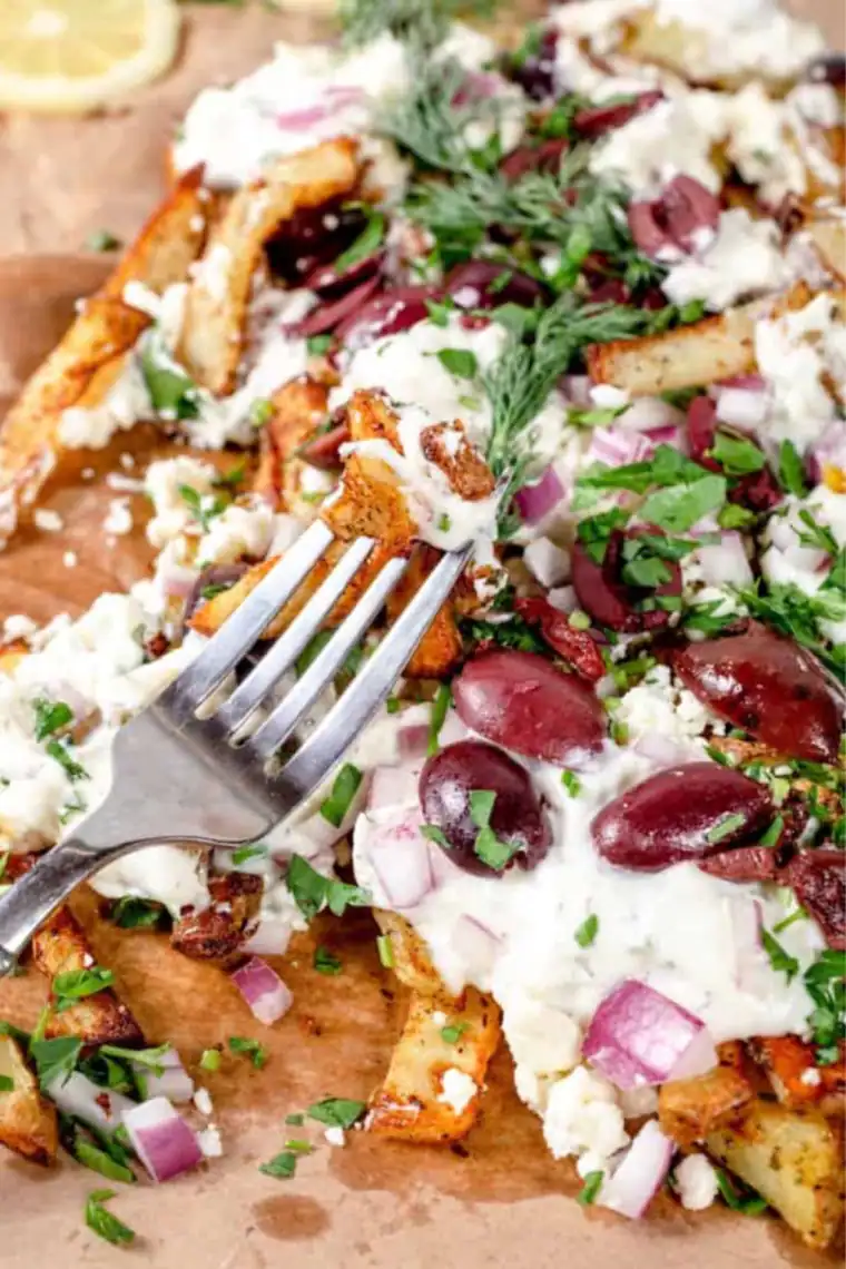 Crispy Air Fryer Greek Fries topped with feta cheese, tomatoes, red onions, and Kalamata olives on a serving plate.