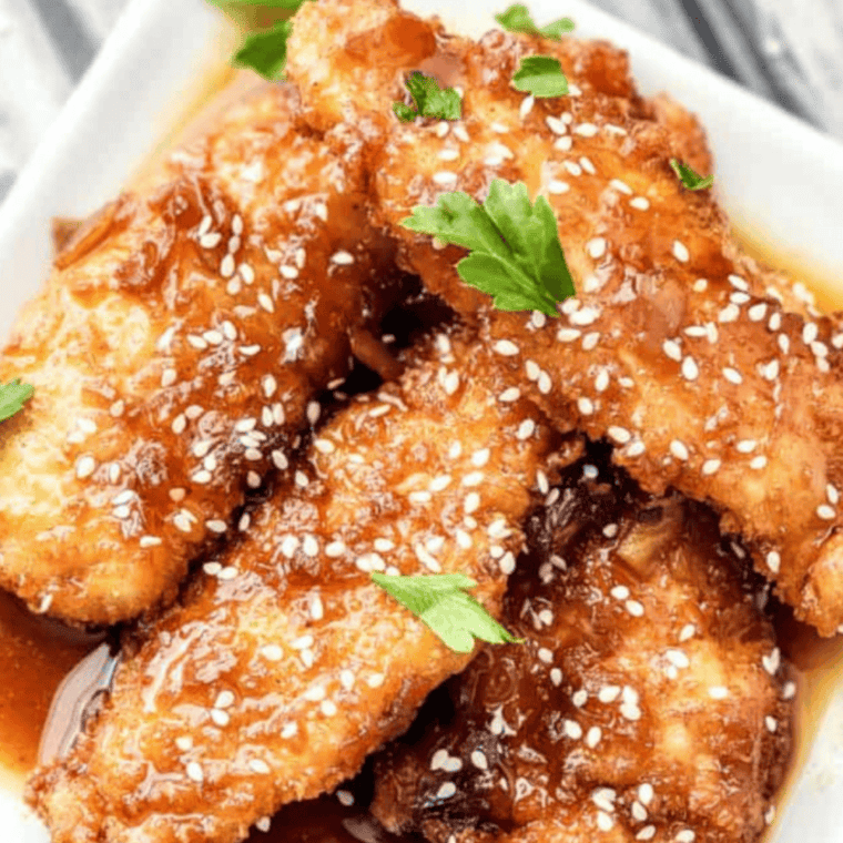 Plate of copycat Jack Daniel's chicken strips in a glossy whiskey glaze, topped with sesame seeds.