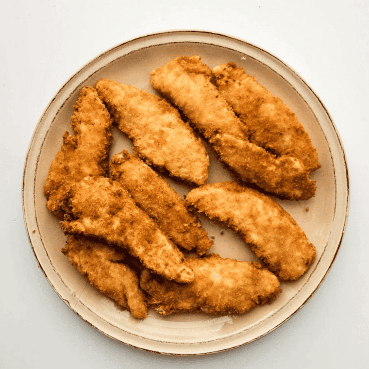 Breaded chicken strips arranged in a single layer in an air fryer basket before cooking.