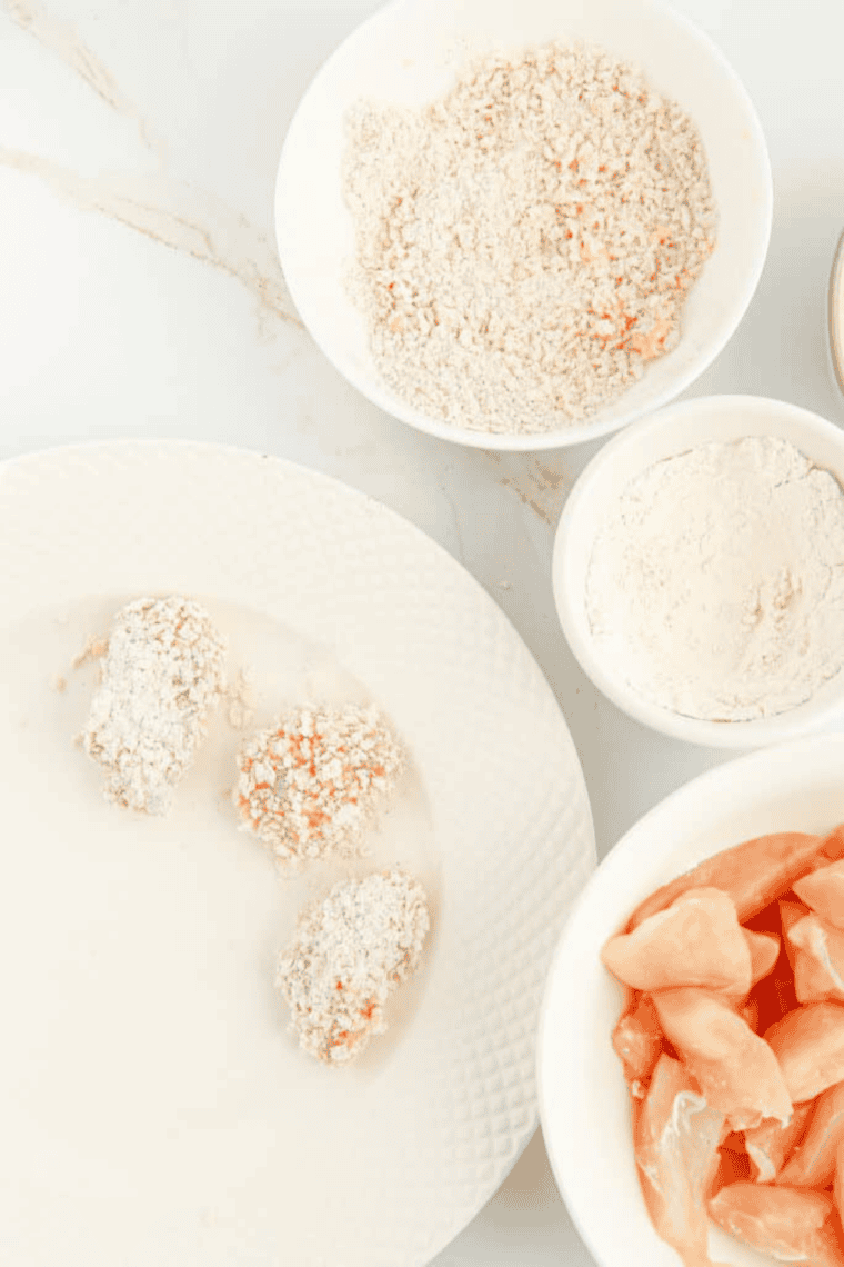 Chicken pieces being dredged in flour, dipped in egg mixture, and coated in seasoned breadcrumbs, then placed on a plate ready for air frying.
